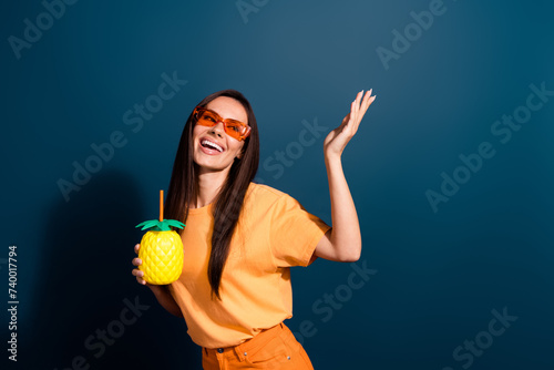 Photo of gorgeous woman dressed yellow t-shirt dancing hold cocktail look at promo empty space isolated on dark blue color background