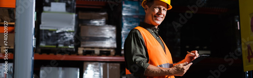 happy middle aged warehouse supervisor in hard hat with clipboard, professional headshots banner