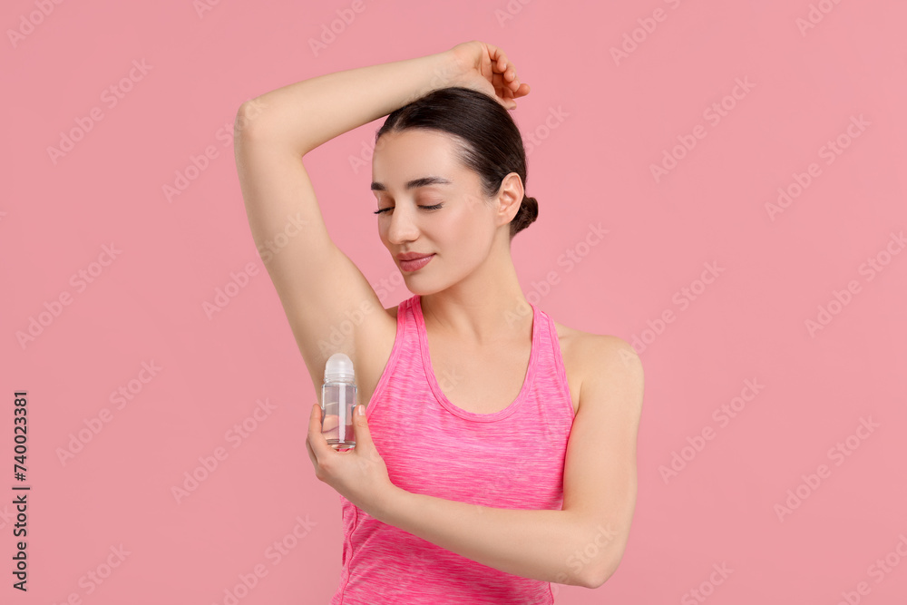Beautiful woman applying deodorant on pink background