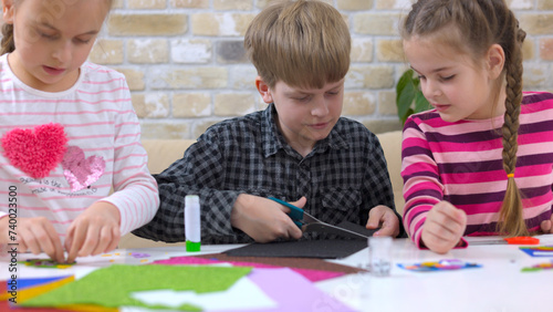 Cute little children cutting color paper with scissors at desk in kindergarten.