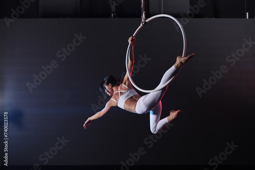 Young woman performing acrobatic element on aerial ring indoors photo