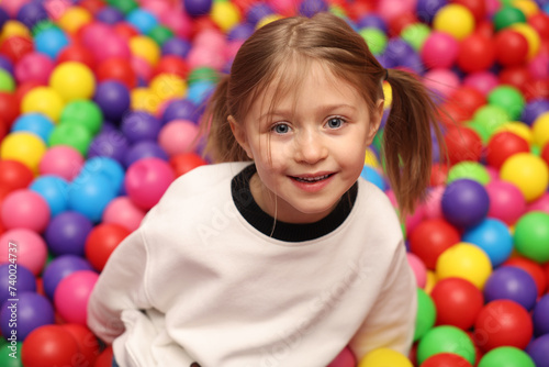 Happy little girl sitting on colorful balls in ball pit