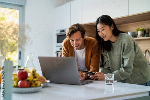 Adult couple shopping online on laptop and smart phone at kitchen counter