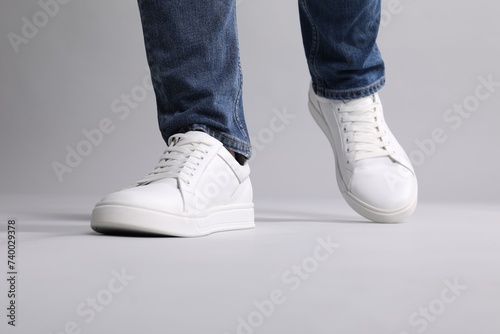 Man wearing stylish white sneakers on grey background, closeup