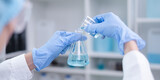 Close-up hands holding pouring blue fluid liquid beaker flask test tube glassware sample laboratory for compare in medicine chemical biology medical medicine science experiment technology analysis