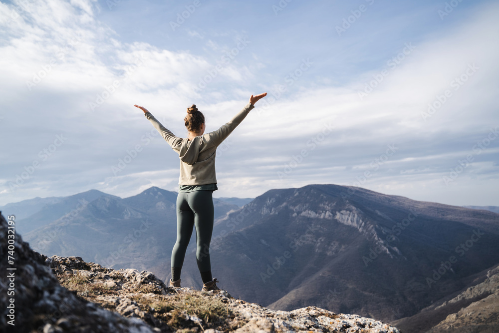 Young cheering woman hiker open arms at mountain peak cliff, fitness girl hiker enjoy the view on mountain top, hiker standing with hands up achieving the top, women enjoy freedom Young cheering woman hiker open arms at mountain peak cliff, fitness girl hiker enjoy the view on mountain top, hiker standing with hands up achieving the top, women enjoy freedom