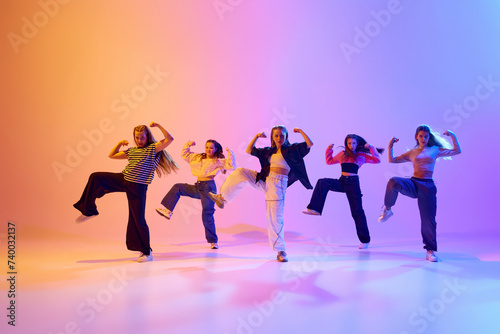 Dynamic image of talented, artistic teen girls dancing hip hop against gradient studio background in neon light. Concept of hobby, youth, childhood, style, fashion, dance school