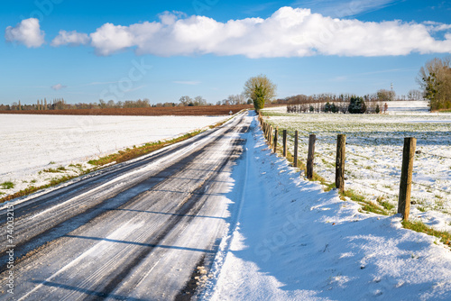 Paysage d'hiver. Route de campagne enneigée avec verglas à travers prairies et champs © S. Leitenberger