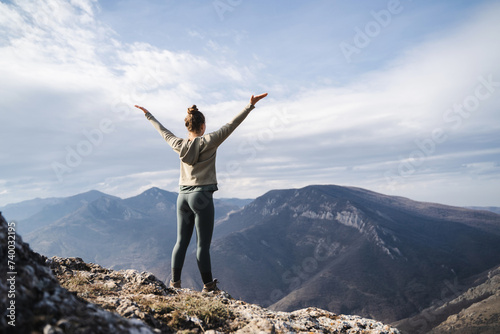 Young cheering woman hiker open arms at mountain peak cliff, fitness girl hiker enjoy the view on mountain top, hiker standing with hands up achieving the top, women enjoy freedom © Соня Монштейн