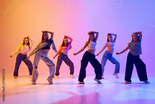 Group of active people, talented dancing hip hop against gradient studio background in neon light. Contemp. Concept of hobby, youth, childhood, style, fashion, dance school photo