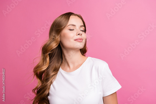 Portrait of peaceful girl with fluttering curly hair dressed white t-shirt close eyes enjoy wind blow isolated on pink color background