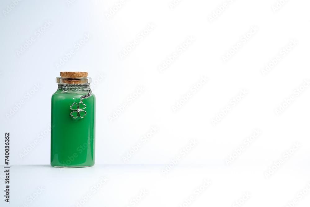Obraz premium Phial with green liquid and four leaf clover shamrock on white background