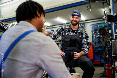 In the workshop's pause, a diverse team of two mechanics shares smiles, stories, and coffee. A scene of unity and friendship beyond the grease and gears.