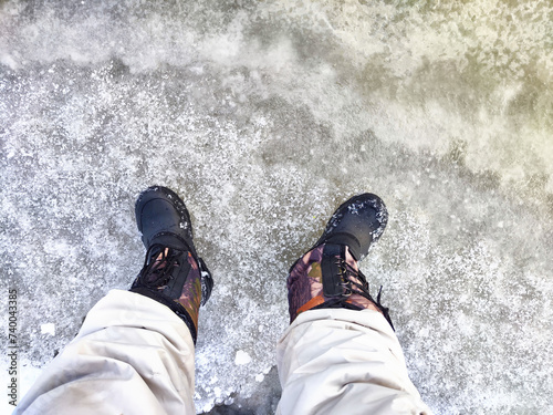 Feet of Hunter or fisherman in big warm boots on a winter day on snow. Top view. Fisherman on the ice of a river, lake, reservoir on spring day with melting ice. Dangerous fishing in spring or autumn