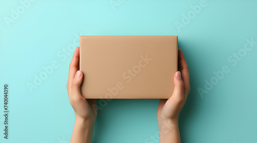 Mockup. Female hand holding brown rectangular cardboard box on blue background, generative ai © Chaman