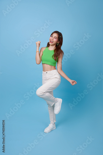 Fototapeta Naklejka Na Ścianę i Meble -  Full length Happy Asian teen girl smiling and jumping while celebrating success isolated on blue background.