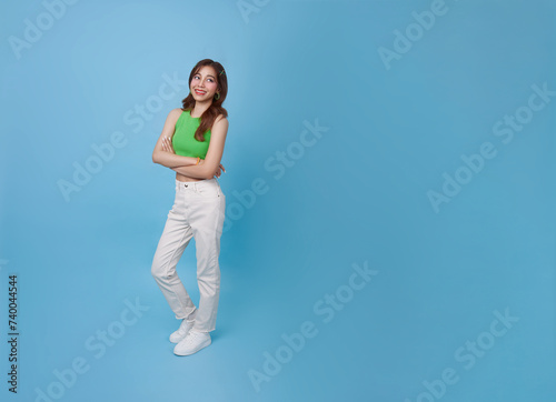 Happy asian teen woman standing with arms crossed and looking up isolated on blue copy space studio background.
