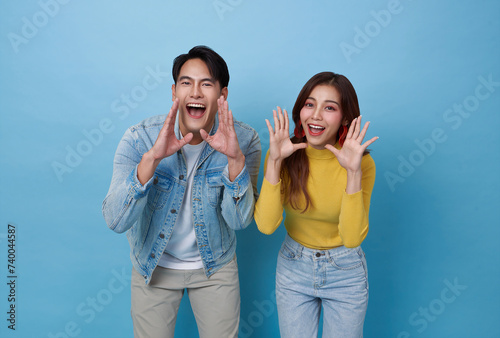 Young lovely asian couple yelling announce with hands cup around mouths isolated on blue studio background.
