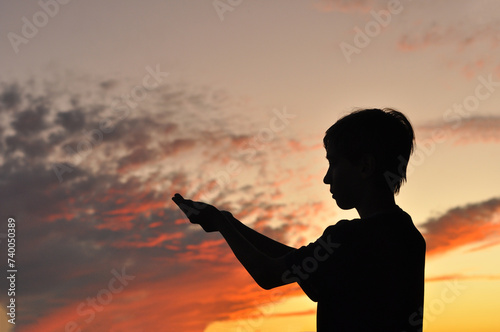 menino em gesto de agradecimento e oração , silhueta em lindo pôr do sol  photo