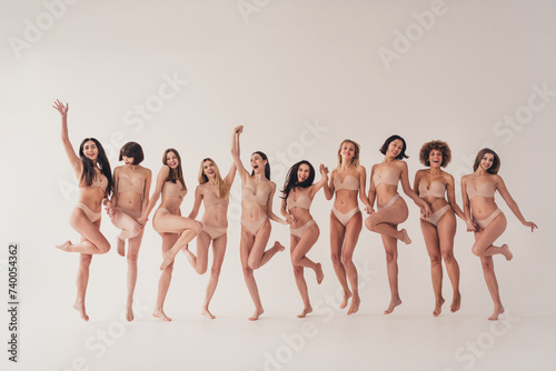 Studio no retouch photo of sweet adorable ladies dressed lingerie jumping holding arms loving themselves isolated beige color wall background