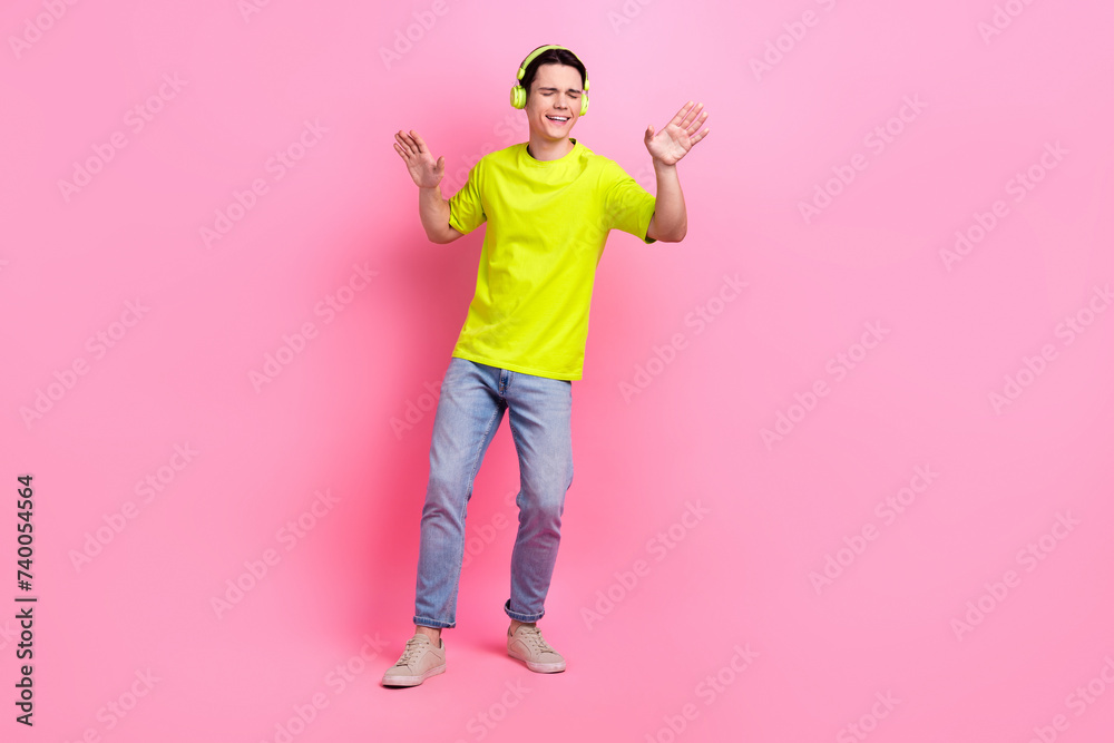 Full length photo of dreamy positive guy wear green t-shirt earphones enjoying songs isolated pink color background Full length photo of dreamy positive guy wear green t-shirt earphones enjoying songs isolated pink color background