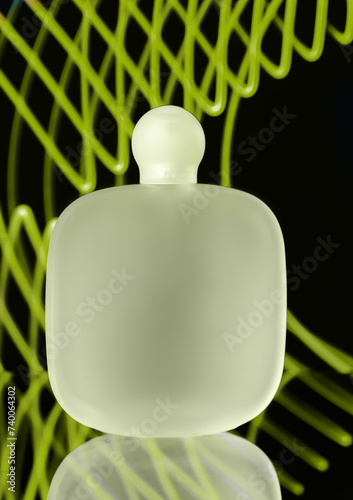 Frosted glass perfume bottle with a rounded cap. The bottle is set against a dynamic background of neon green lines creating an abstract pattern. 