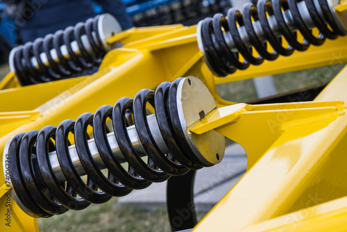 Steel black spring as part of yellow agricultural machine. Technology