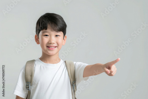 a boy with an Asian appearance in a white T-shirt with a briefcase, a schoolboy, smiling, pointing to the side, on a gray background