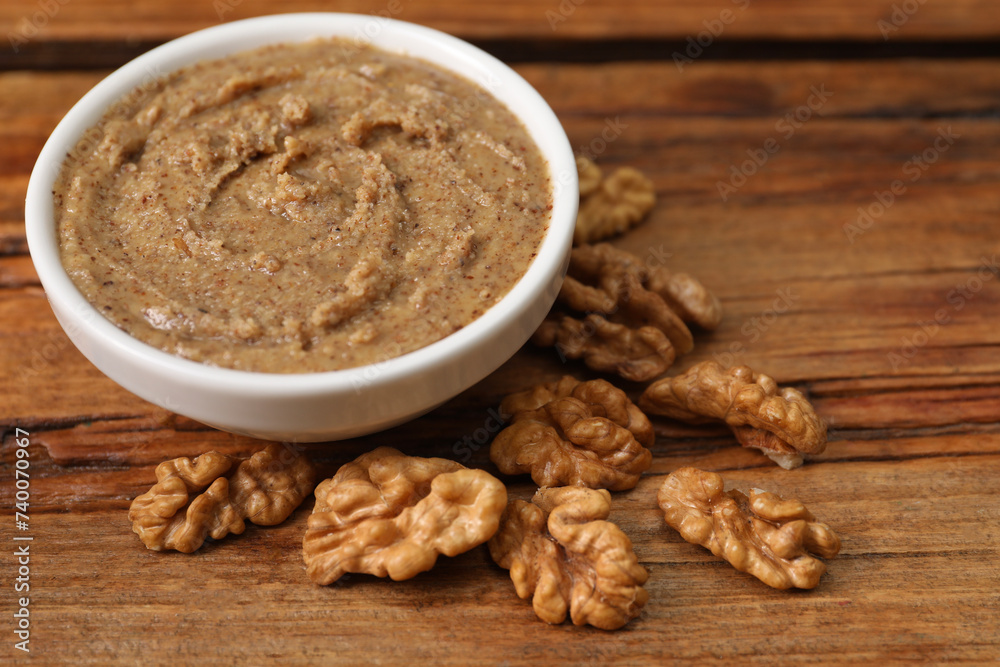 Delicious nut butter in bowl and walnuts on wooden table, closeup Delicious nut butter in bowl and walnuts on wooden table, closeup