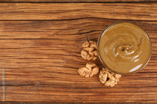 Delicious nut butter in bowl and walnuts on wooden table, top view. Space for text