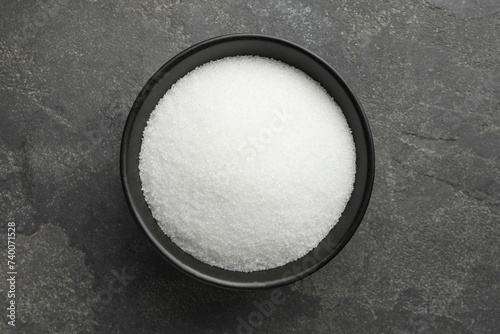 Granulated sugar in bowl on grey textured table, top view photo