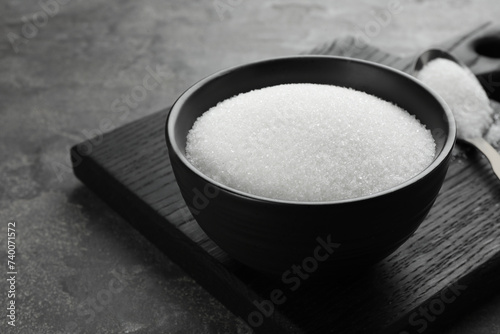 Granulated sugar in bowl on grey textured table, closeup. Space for text