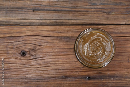 Tasty nut paste in jar on wooden table, top view. Space for text