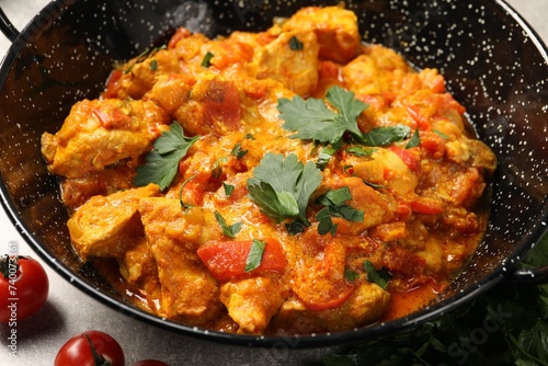 Delicious chicken curry in frying pan and tomatoes on table, closeup