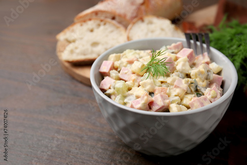 Tasty Olivier salad with boiled sausage in bowl on wooden table, space for text