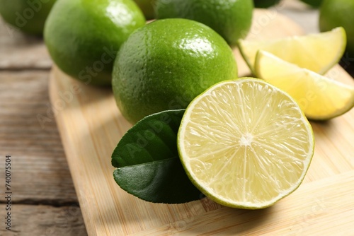 Whole and cut fresh limes on wooden table, closeup