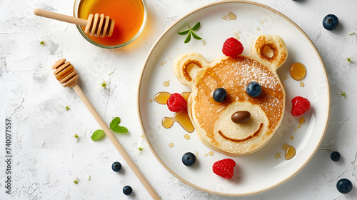 children's breakfast pancakes in the shape of a cute bear's face with berries and honey on a light background, top view with copy space for recipe