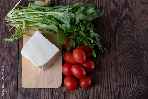 Ingredients for salad, fresh arugula, cheese and cherry tomatoes on a wooden table.