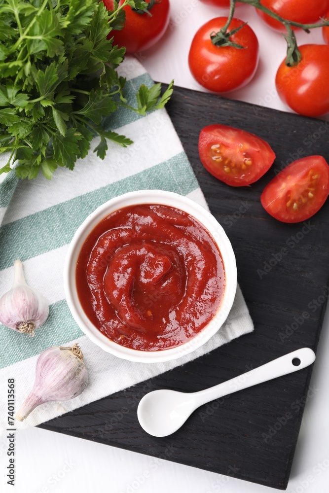 Organic ketchup in bowl, fresh tomatoes, parsley and garlic on white table, flat lay. Tomato sauce Organic ketchup in bowl, fresh tomatoes, parsley and garlic on white table, flat lay. Tomato sauce