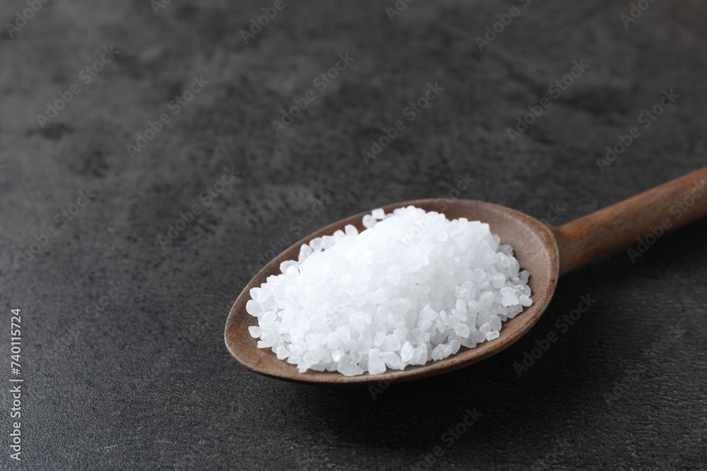 Natural salt in wooden spoon on dark grey table, closeup. Space for text Natural salt in wooden spoon on dark grey table, closeup. Space for text