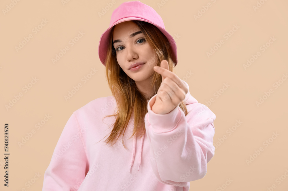 Young woman making heart with her fingers on beige background Young woman making heart with her fingers on beige background