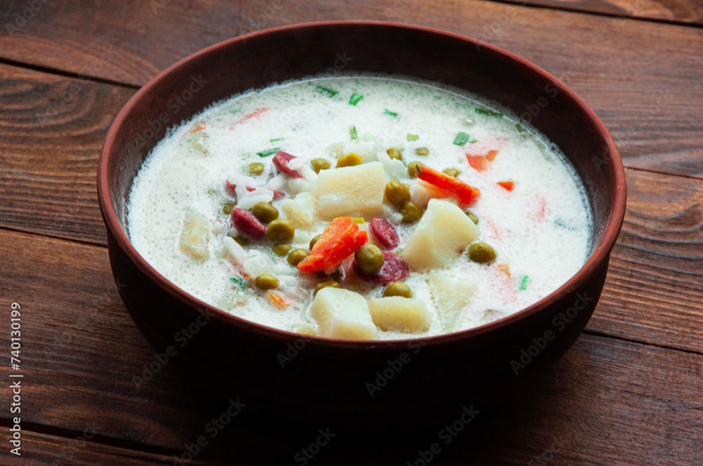 cheese soup in a clay plate on a wooden background. soup with young vegetables on a brown table. home cooking concept	