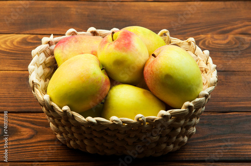 redsided apples in a wicker basket on a wooden background. sweet yellow apples on a brown texture photo