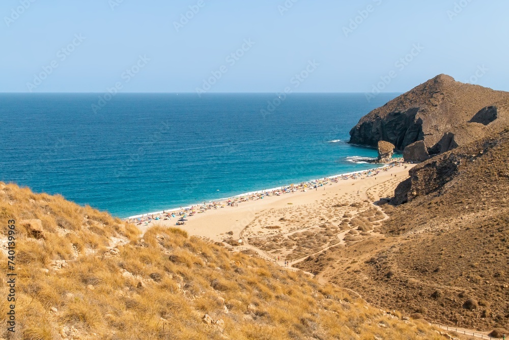 Bañistas tomando el sol en la playa de Los Muertos, Carboneras, Almería, España. Vista cenital de la playa a orillas del mar Mediterráneo con sus aguas turquesas un soleado día de verano.
