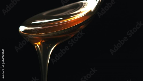 Cuchara vertiendo miel con fondo negro. Líquido marrón viscoso que cae suavemente. Textura liquida. Macro 60fps 4k photo