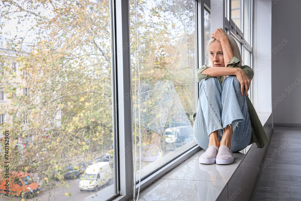 Fototapeta premium Depressed mature woman sitting near window at home
