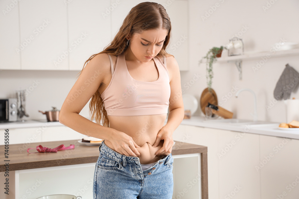 Young woman in tight jeans at home. Weight gain concept Young woman in tight jeans at home. Weight gain concept