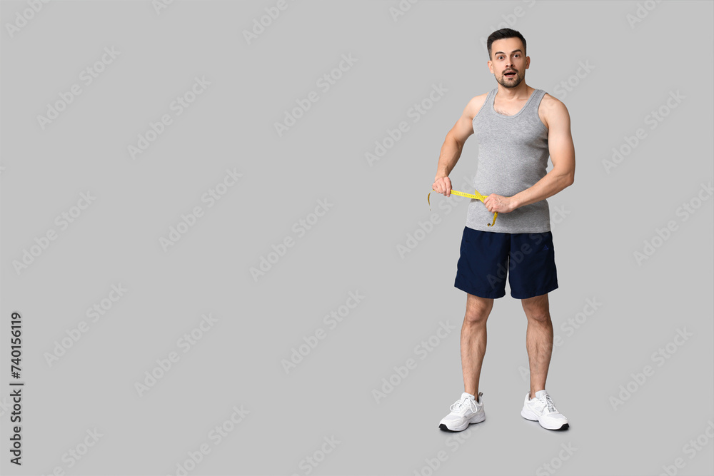 Handsome sporty shocked man measuring his waist on grey background. Weight loss concept Handsome sporty shocked man measuring his waist on grey background. Weight loss concept