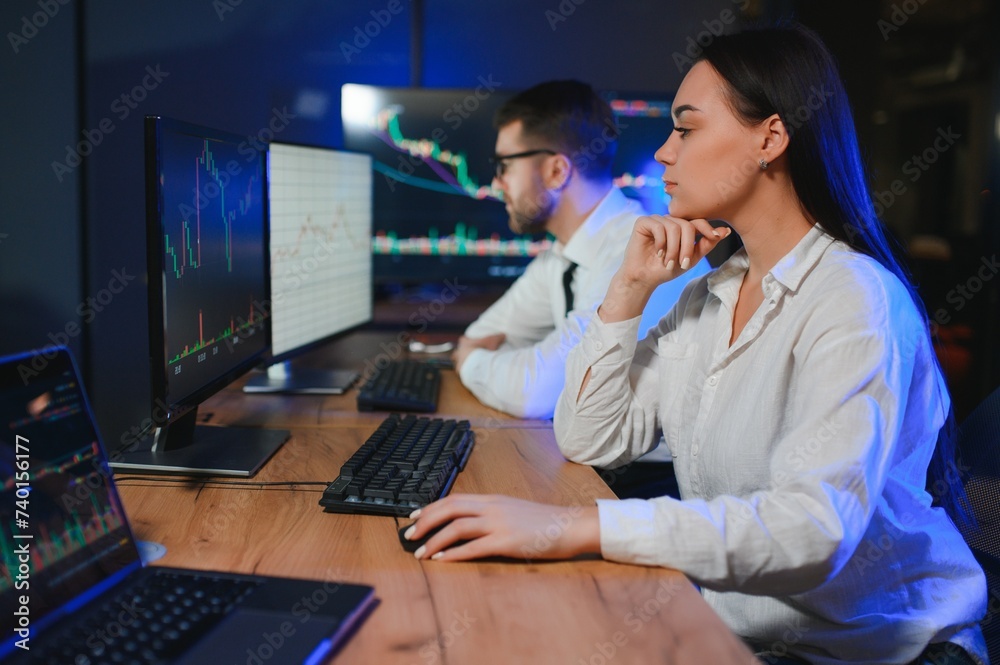 Team of stockbrokers are having a conversation in a dark office with display screens Team of stockbrokers are having a conversation in a dark office with display screens
