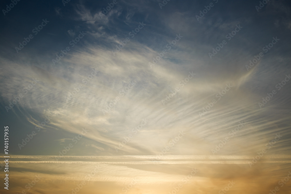 Sunset sky, clouds illuminated by the sun. Contrails and feather clouds.